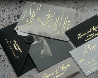 May include: Wedding invitation suite with black and gray envelopes, a clear vellum invitation with gold foil lettering, and a gray RSVP card with gold foil lettering. The invitation text reads "Emma & Kevin" and the RSVP card text reads "RSVP by 15th of April, 2023".