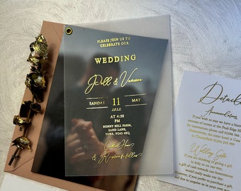 May include: A wedding invitation on a clear acrylic card with gold lettering. The invitation reads "Please join us to celebrate our wedding Pell & Vamm Sunday 11 May 2022 at 4:30 PM Bunny Hill Farm, Sand Lane, York, YO4S 4XQ.  Celebrant: Rev.  Reception to follow."