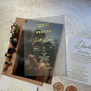May include: A wedding invitation on a clear acrylic card with gold lettering. The invitation reads "Please join us to celebrate our wedding Pell & Vamm Sunday 11 May 2022 at 4:30 PM Bunny Hill Farm, Sand Lane, York, YO4S 4XQ.  Celebrant: Rev.  Reception to follow."