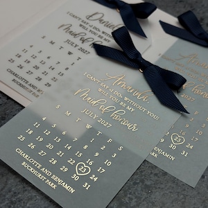 May include: A light blue and white card with gold lettering that says "I can't say I do without you! Will you be my Maid of Honour?" with a calendar showing July 2027 with the 23rd circled.