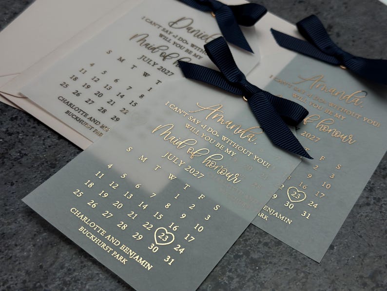 May include: A light blue and white card with gold lettering that says "I can't say I do without you! Will you be my Maid of Honour?" with a calendar showing July 2027 with the 23rd circled.