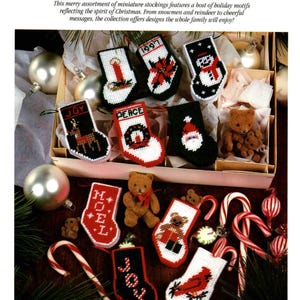 May include: A collection of miniature needlepoint Christmas stockings featuring various holiday motifs including a snowman, Santa Claus, a cardinal, a candle, a wreath, and the words JOY, PEACE, and NOEL, displayed with small teddy bears and candy canes.