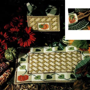 以下が含まれることがあります： 秋をテーマにした装飾セット。かぼちゃのモチーフが施された織りバスケットとプレースマット。バスケットとプレースマットはベージュとグリーンの配色です。画像には赤い花、トウモロコシ、ヒマワリも含まれています。