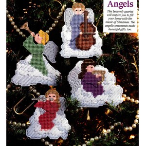 May include: Four cross-stitch angel ornaments on white clouds, each playing a different instrument: a trumpet, cello, harp, and flute. The text reads: Band of Angels. This heavenly quartet will inspire you to fill your home with the music of Christmas.