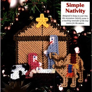 May include: A plastic canvas nativity ornament featuring a tan stable with a yellow star, a blue figure, a red figure, a white figure in a dark brown manger, a black and white animal, and a tan camel with red and blue accents. Text reads Simple Nativity.