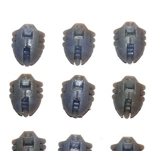 May include: A collection of twenty dark gray plastic components, each with a unique, symmetrical design featuring a central rectangular indentation and multiple small, curved protrusions. The components are arranged in a grid pattern against a white background.