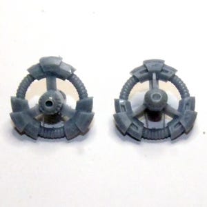 May include: Two gray, plastic, circular components with a central hub and radiating arms. Each component has a ring-like structure with a series of rectangular blocks and a central, circular feature. The components appear to be parts of a larger mechanism.