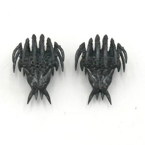 May include: Two dark gray, claw-shaped decorative objects. Each claw has multiple pointed fingers and a textured surface. The claws are symmetrical and appear to be made of metal or a similar material. The background is plain white.