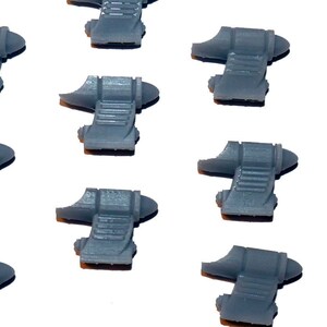 May include: A collection of nine gray, 3D-printed miniature components, each with a unique shape featuring a curved top and a stepped, rectangular base. One component is oriented horizontally. The objects are arranged on a white background.