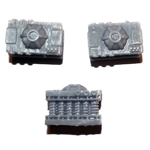 May include: Three small, gray, rectangular components with intricate details. Two components have a circular design on top, while the third component is viewed from the side, revealing a layered structure. The objects appear to be miniature models or parts.