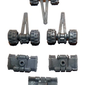May include: A collection of gray plastic toy parts, including wheel assemblies and rectangular components. The wheels have a textured design. The parts are arranged against a white background.