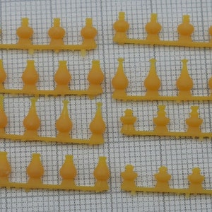 May include: A sheet of yellow plastic lamp finials, arranged in rows. The finials are shaped like small, round bottles with a pointed top.