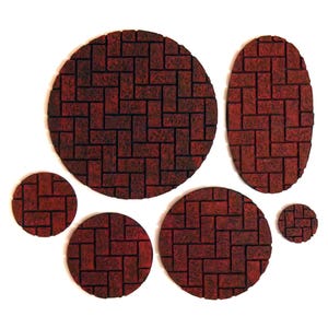 May include: A collection of seven red brick-patterned coasters in various shapes and sizes. The coasters include two circles, two smaller circles, an oval, and a small circle. The brick pattern is dark red with black grout lines.