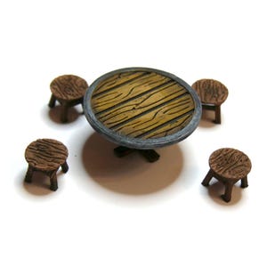 May include: A miniature wooden table with a round top and four matching stools. The table has a light brown, wood-grain surface with a gray rim. The stools are small, with three legs each, and have a similar wood-grain design. The set is designed for a dollhouse or miniature setting.