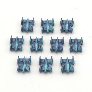 May include: Ten small, teal and purple spaceship miniatures arranged on a white surface. Each miniature has a distinct, detailed design with wings and a central body. The color scheme is a blend of teal and purple.