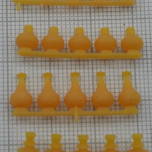 May include: A sheet of clear plastic with 30 small, yellow, plastic, bottle-shaped objects attached. The objects are arranged in four rows of seven, eight, eight, and seven objects.