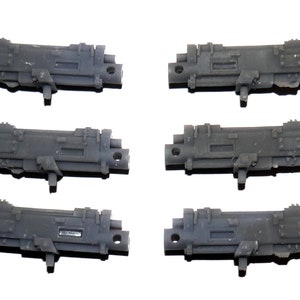 May include: Six gray plastic miniature gun models. Each model has a rectangular body with detailed mechanical features, including protruding elements and a small, cylindrical barrel. The models are designed for hobby or gaming purposes.