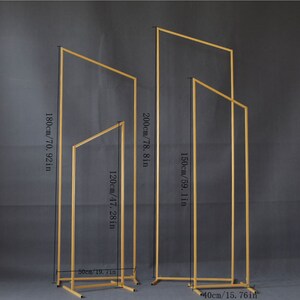 May include: Four gold metal arch stands of varying heights. The tallest is 200 cm high, and the shortest is 120 cm high. The stands are rectangular with a square base, suitable for weddings or events.