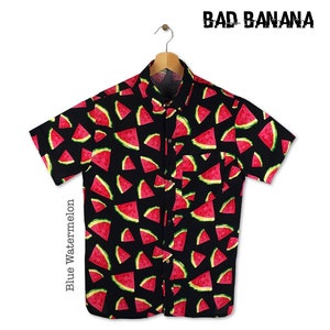 Puede incluir: Una camisa negra de manga corta con botones y estampado de sandía. La camisa tiene un bolsillo en el lado izquierdo y el texto "BAD BANANA" está impreso en la parte superior de la imagen. El texto "Blue Watermelon" está impreso en el lado izquierdo de la imagen.