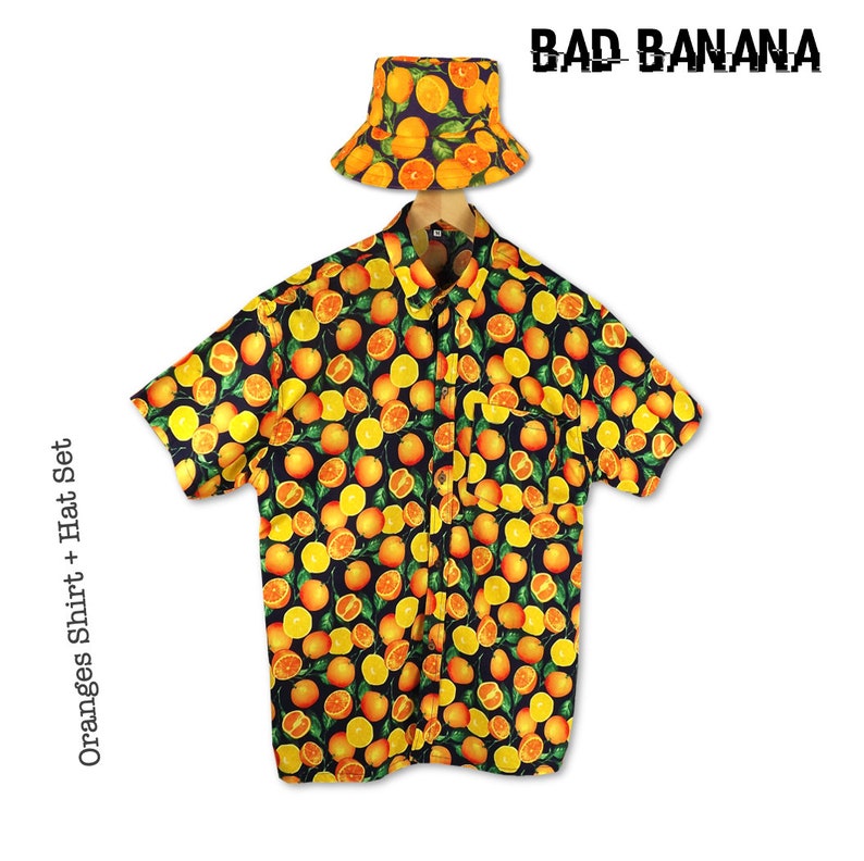 May include: A black button-up shirt with a short sleeve and an all-over orange print. The shirt has a pocket on the left side. A matching orange bucket hat with green leaves is included. The text "BAD BANANA" is printed in white on a black background. The text "Oranges Shirt + Hat Set" is printed on the left side of the image.
