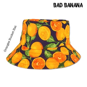 May include: A blue bucket hat with an orange and green print of oranges. The hat has the text "BAD BANANA" in white letters on the top and "Oranges Bucket Hat" in white letters on the side.