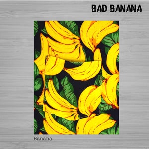 Pu&ograve; includere: Un tessuto nero con un motivo ripetuto di banane gialle e foglie verdi. Il testo "BAD BANANA" &egrave; stampato in bianco nella parte superiore del tessuto. Il testo "Banana." &egrave; stampato in bianco nella parte inferiore del tessuto.