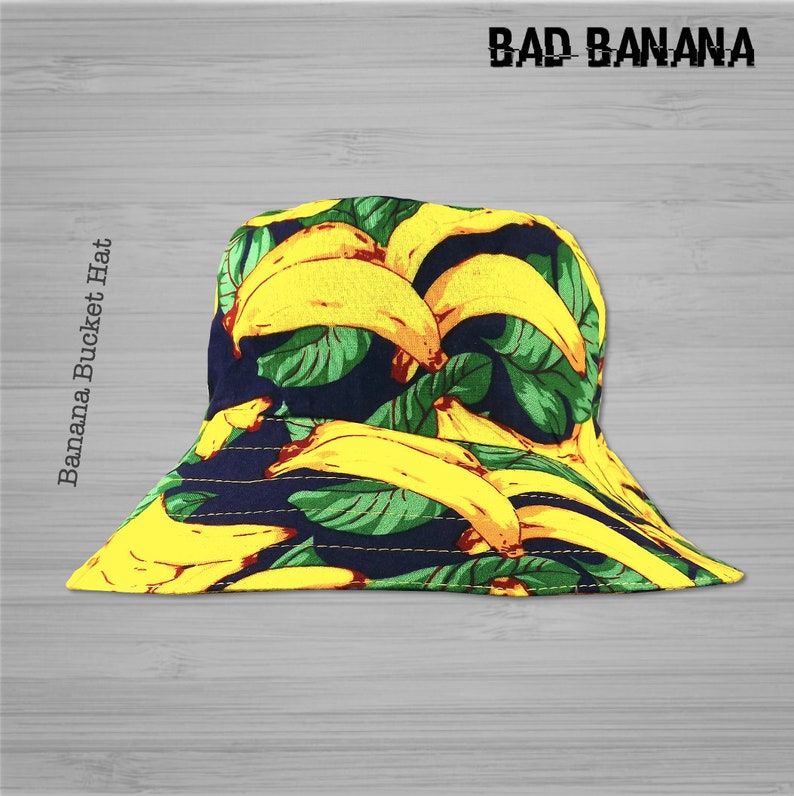Pu&ograve; includere: Un cappello a secchiello giallo e verde con una stampa di banana. Il cappello ha il testo "BAD BANANA" stampato sul davanti.
