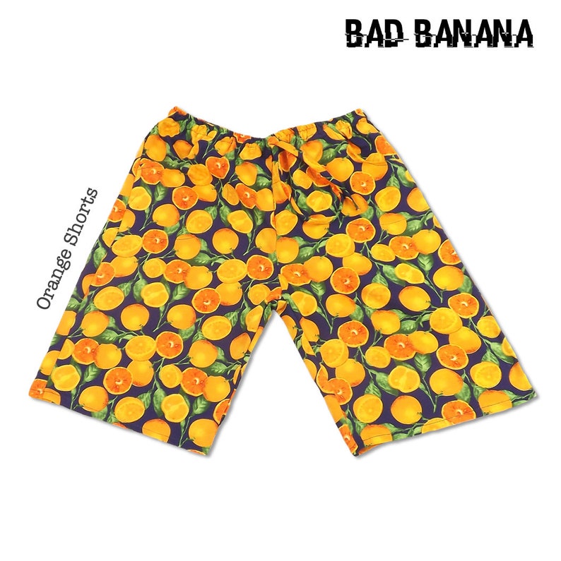 May include: Orange shorts with a navy blue background and a repeating pattern of yellow oranges with green leaves. The text "BAD BANANA" is printed in white at the top of the image.
