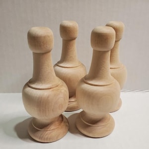 May include: Four unfinished wooden finials with a bulbous shape and a rounded top. The finials are arranged in a semi-circle on a white surface.