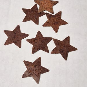 May include: Seven rustic, brown metal stars of various sizes. The stars are scattered on a white surface.