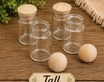 May include: Four small clear glass jars with light-colored wooden lids. Two jars are capped with lids, while two are open. Two smooth wooden spheres are placed in front of the jars. A rectangular label with the word Tall is centered below.