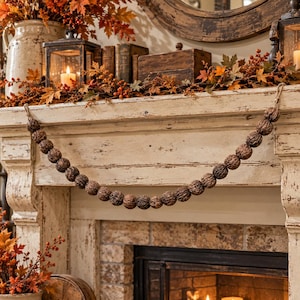 May include: A decorative garland composed of numerous brown, textured walnut shells strung together on a thin cord. The garland is draped horizontally across the front of a distressed, off-white wooden fireplace mantel.