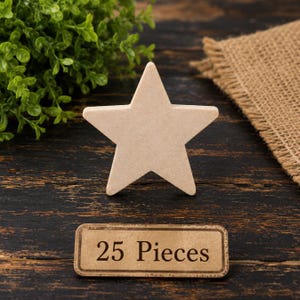 May include: A light beige, five-pointed star cutout made of smooth, flat material. Below the star is a rectangular label with a brown border and a light tan background, featuring the black printed text 25 Pieces in a serif font.