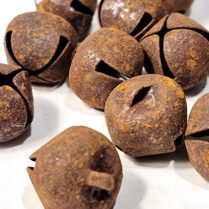 May include: A group of ten rusty metal jingle bells. The bells are all different sizes and shapes, but they all have a similar design. They are all a dark brown color with a lot of rust on them.