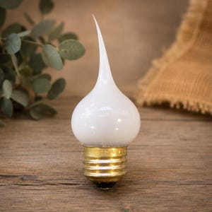 May include: A white frosted glass light bulb with a flame-shaped tip and a brass-colored metal screw base. The bulb features a rounded body that tapers into a pointed, curved top, providing a distinct silhouette for decorative lighting fixtures.