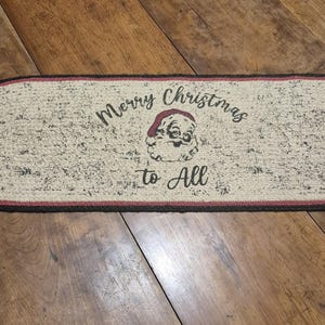 May include: A beige oval-shaped doormat with a red border and black trim. The doormat has a black and white image of Santa Claus with the text "Merry Christmas to All".