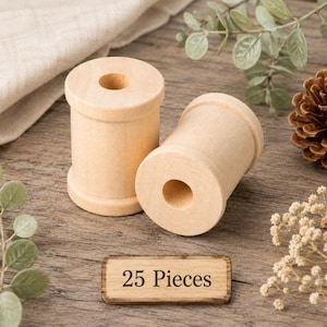 May include: Two cylindrical light-colored wooden spools with a smooth finish and a central hole running through each piece. A small rectangular wooden sign is placed in front of the spools with the text 25 Pieces printed in black ink.