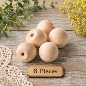 May include: A set of six light-colored, unfinished wooden spheres, each featuring a centered circular hole. The items are arranged in a cluster, accompanied by a small rectangular wooden plaque engraved with the text 6 Pieces.