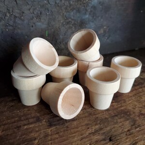 May include: A group of small, unfinished wooden plant pots. The pots are arranged in a pile, with some of them stacked on top of each other. The pots are all the same size and shape, and they have a smooth, natural finish.