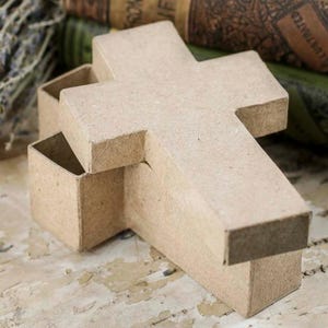 May include: A cross-shaped box made of light brown, textured paperboard material. The container consists of a base and a removable lid, both featuring a matte finish and a simple, geometric design shaped like a traditional cross with straight edges.