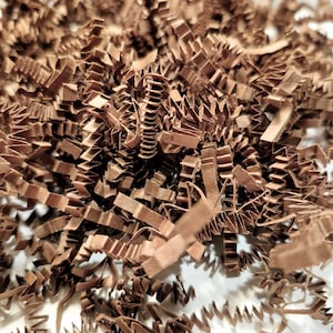 May include: Brown paper crinkle cut shredded packing material. This is a close-up of the shredded paper, which is often used for packaging gifts and other items.