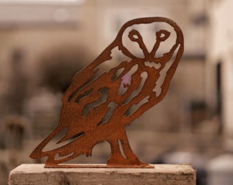 May include: A rusty brown metal sculpture of a barn owl with detailed feathers and eyes. The sculpture is standing on a light brown surface.
