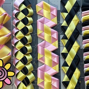 May include: Close-up of several colorful ribbon designs. The ribbons are in various patterns, including zigzags and diamond shapes, and feature combinations of pink, yellow, and black. A flower graphic is in the lower left corner.