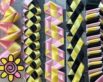 Può includere: Primo piano di diversi disegni di nastri colorati. I nastri sono in vari modelli, tra cui zigzag e forme a diamante, e presentano combinazioni di rosa, giallo e nero. Una grafica floreale si trova nell'angolo in basso a sinistra.