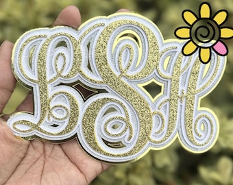 Può includere: Un monogramma dorato, bianco e glitterato con le lettere LSA. Il monogramma è tenuto in mano e presenta un girasole decorativo nell'angolo in alto a destra. Le lettere sono stratificate con un centro glitterato dorato.