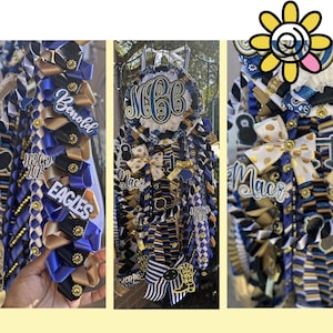 Puede incluir: Mums de bienvenida en azul, dorado y negro. Las mums presentan cintas, lazos y etiquetas de nombre personalizadas. Algunas tienen los nombres "Benold" y "Maci".