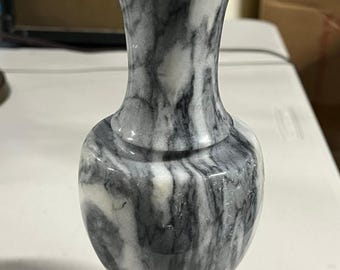 May include: A decorative marble vase with a flared top and a rounded body. The vase features a gray and white marbled pattern. The vase is a decorative item for the home.