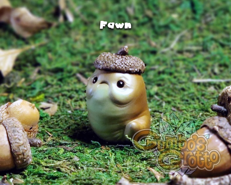 May include: A small, brown, ceramic figurine of a fawn wearing an acorn hat. The figurine is sitting on a bed of green moss.