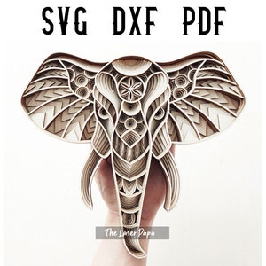 May include: A detailed, layered wooden elephant head with intricate geometric patterns. The elephant's head is carved in a mandala style, with a flower design in the center of its forehead. The image includes the text "The Laser Papa".