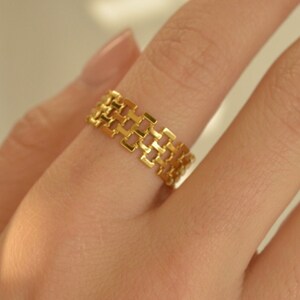 May include: A gold ring with a geometric design. The ring is made of a series of interlocking squares.